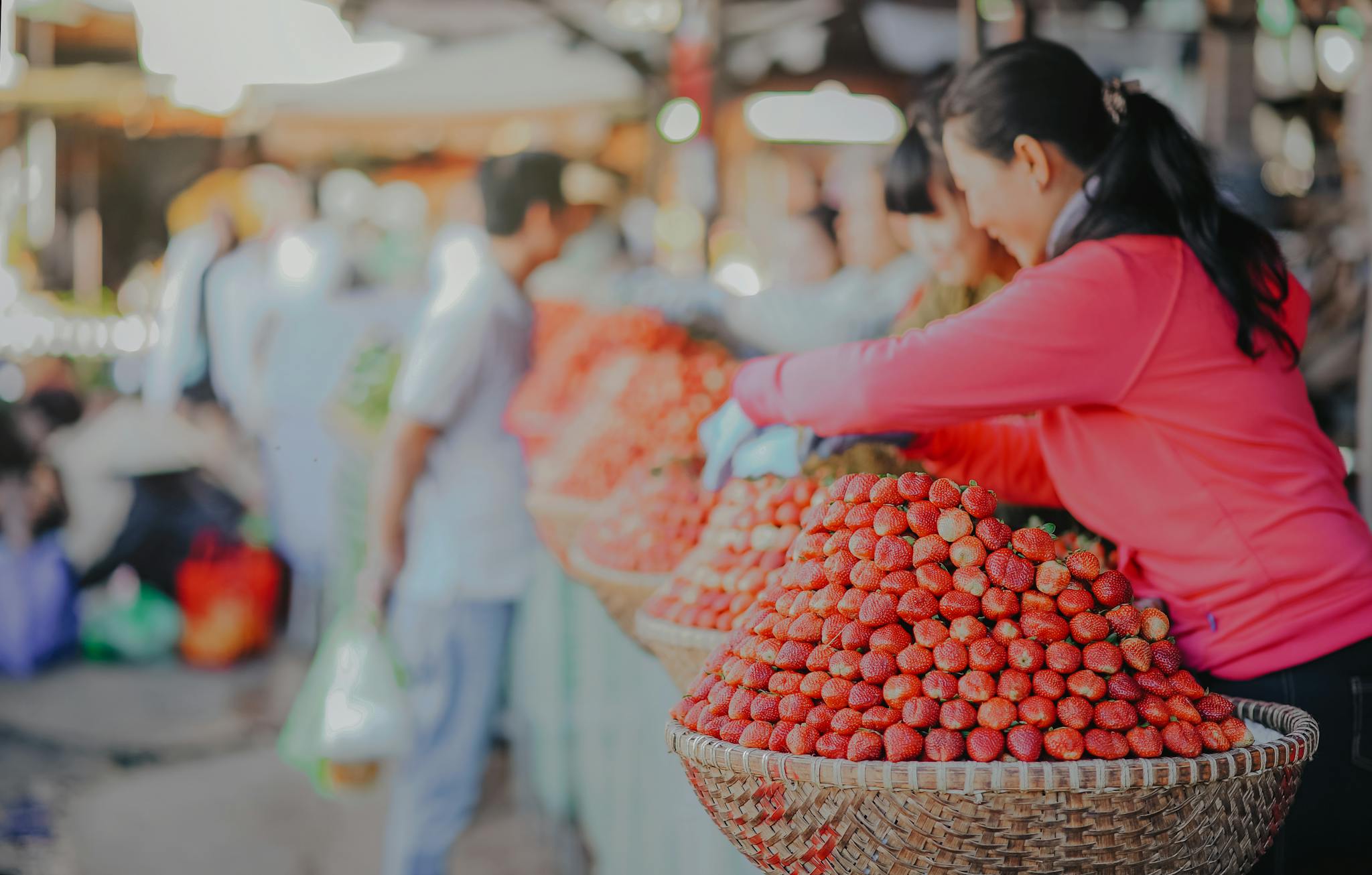 Woman selling fresh strawberries at an outdoor market stall during the day.